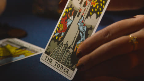 Nahaufnahme-Einer-Frau,-Die-Auf-Einem-Kerzenbeleuchteten-Tisch-Tarotkarten-Liest-Und-Die-Turmkarte-2-Hält